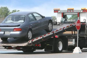 Blue sedan being loaded onto flatbed tow truck for auto transport service