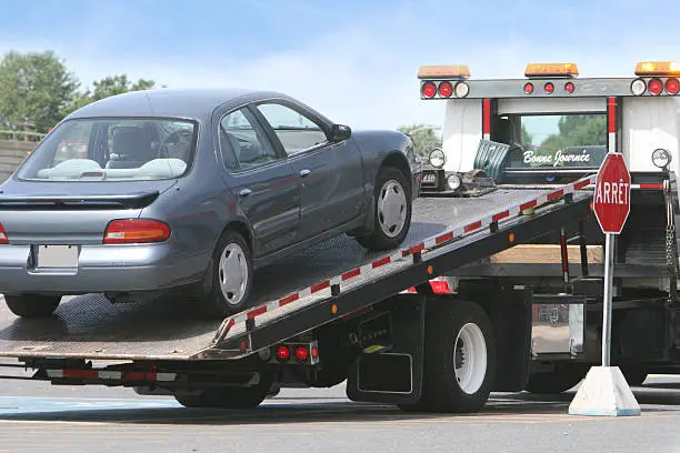 Blue sedan being loaded onto flatbed tow truck for auto transport service